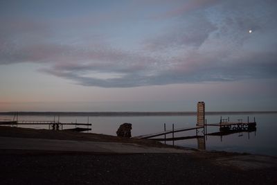 Pier over river against cloudy sky at dusk