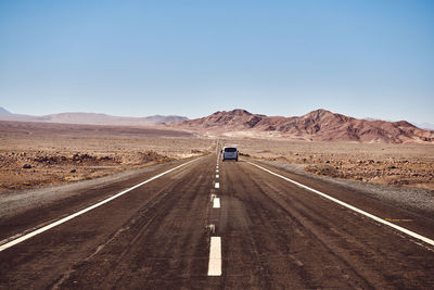 Road passing through desert against clear sky