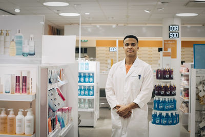 Portrait of confident owner wearing lab coat standing in pharmacy store