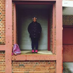 Full length portrait of student standing against closed shutter in building at campus