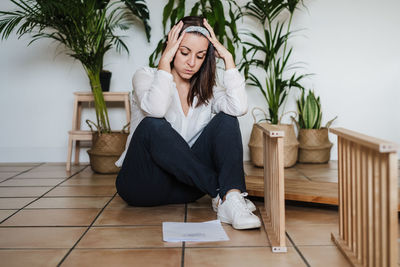 Young woman sitting on potted plant at home