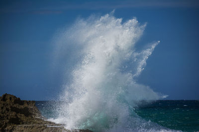 Waves splashing on shore against blue sky