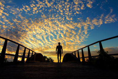 Silhouette man standing on bridge against sky during sunset