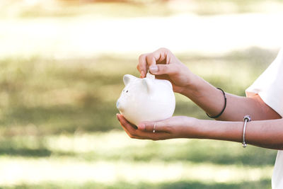 Cropped image of woman inserting coin in piggy bank outdoors