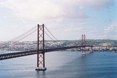 Suspension bridge over sea against cloudy sky