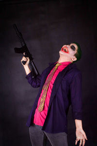 Smiling young man with gun wearing costume against black background