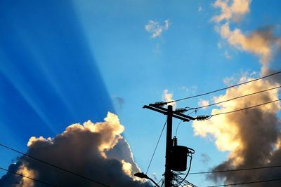 Low angle view of silhouette electricity pylon against blue sky