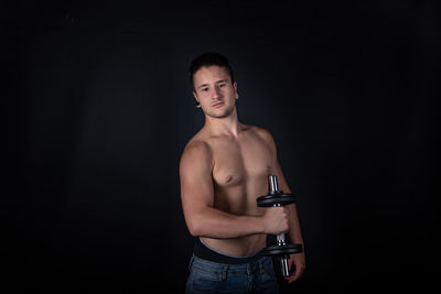 Portrait of shirtless man standing against black background