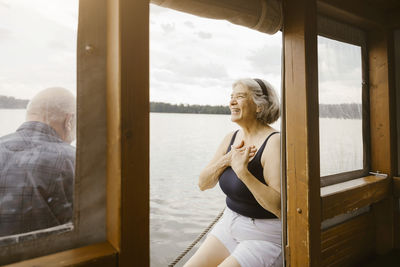 Happy senior woman with hands on chest sitting near man at houseboat