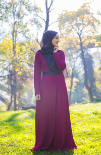 Young woman standing by tree on field