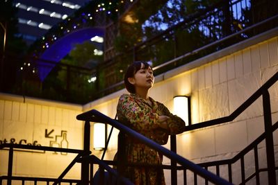 Young woman looking away while standing against railing