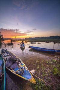 Fishing boat moored at beach against sky during sunset