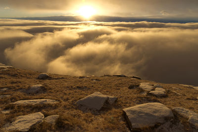 Scenic view of rocks and sea of clouds against sky during sunset