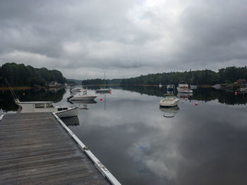 Boats moored in lake against cloudy sky