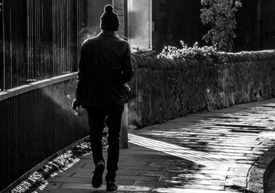 Rear view of man walking on footpath in city