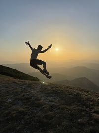 Rear view of woman standing on rock against sky during sunset