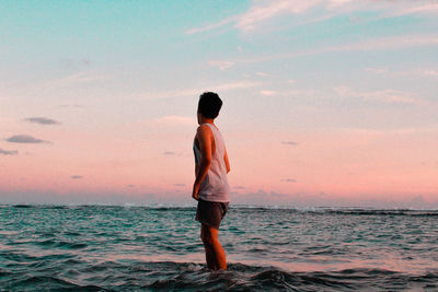 Rear view of boy standing on beach against sky during sunset