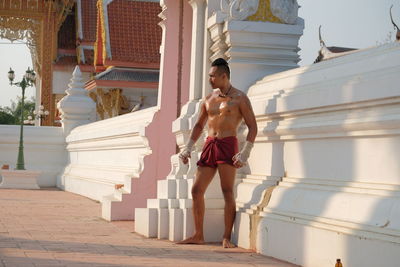 Full length of shirtless man standing against building