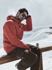 Man sitting on railing against snow covered landscape