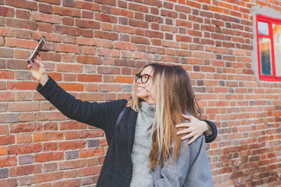 Female friends taking selfie against wall