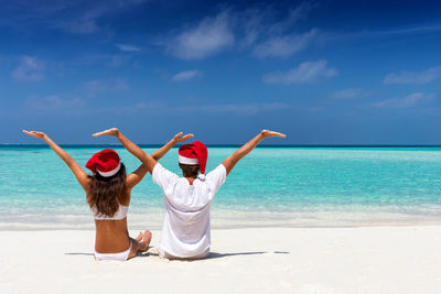 People in santa hat sitting at beach against sky