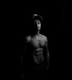 Portrait of shirtless man standing against black background