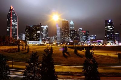 Illuminated city seen from park against sky at night