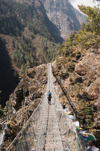 Rear view of man walking on footbridge against mountain