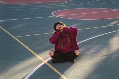 Full length of young woman sitting on basketball court