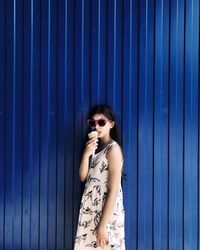 Young woman wearing sunglasses standing against blue wall