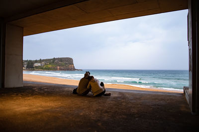 Woman sitting on shore at beach against sky