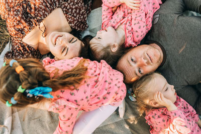 Happy family with triplet girls is lying in park, relaxing in the outdoors
