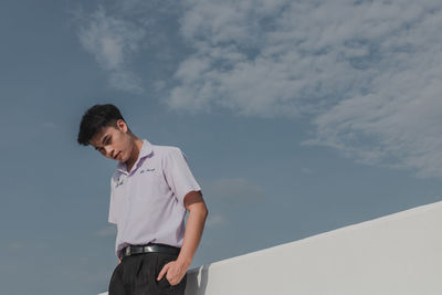 Low angle view of young man looking away against sky