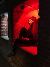 Woman sitting against red wall