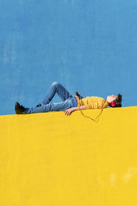 Full length of boy lying down while listening music against wall