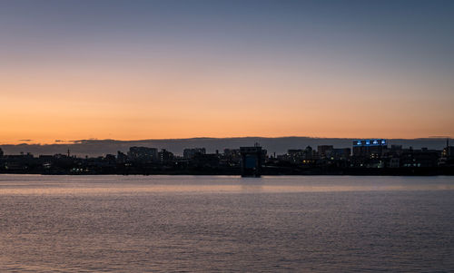 Silhouette buildings by sea against romantic sky at sunset