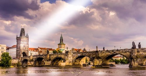 Arch bridge over river amidst buildings against sky