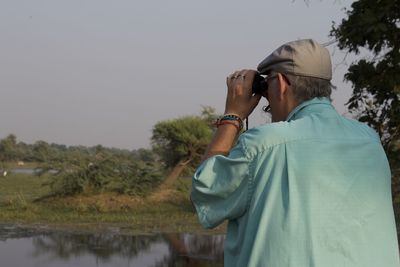 Man photographing on mobile phone against sky
