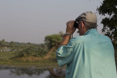 Man looking through binoculars against sky