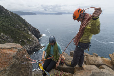 Men fishing on rock by sea against sky