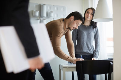 Woman looking at real estate agent while man signing documents at new home