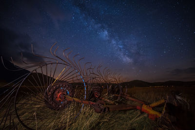 Abandoned machinery on grassy field against star field at night