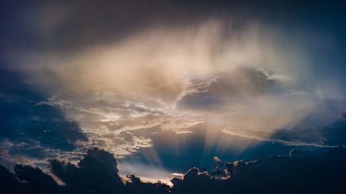 Low angle view of sunlight streaming through clouds