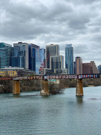 Modern buildings by river against sky in city