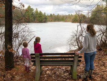 Rear view of women standing on bench by lake