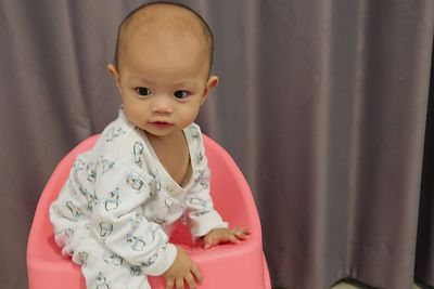 Cute baby boy sitting on seat against curtain at home