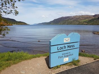 Information sign by lake against sky