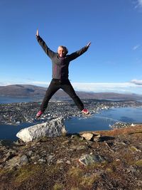 Portrait of man with arms outstretched jumping against townscape and lake