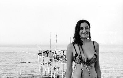 Portrait of smiling young woman standing at beach against clear sky