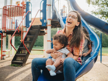 Smiling mother with cute kid sitting on slide at park